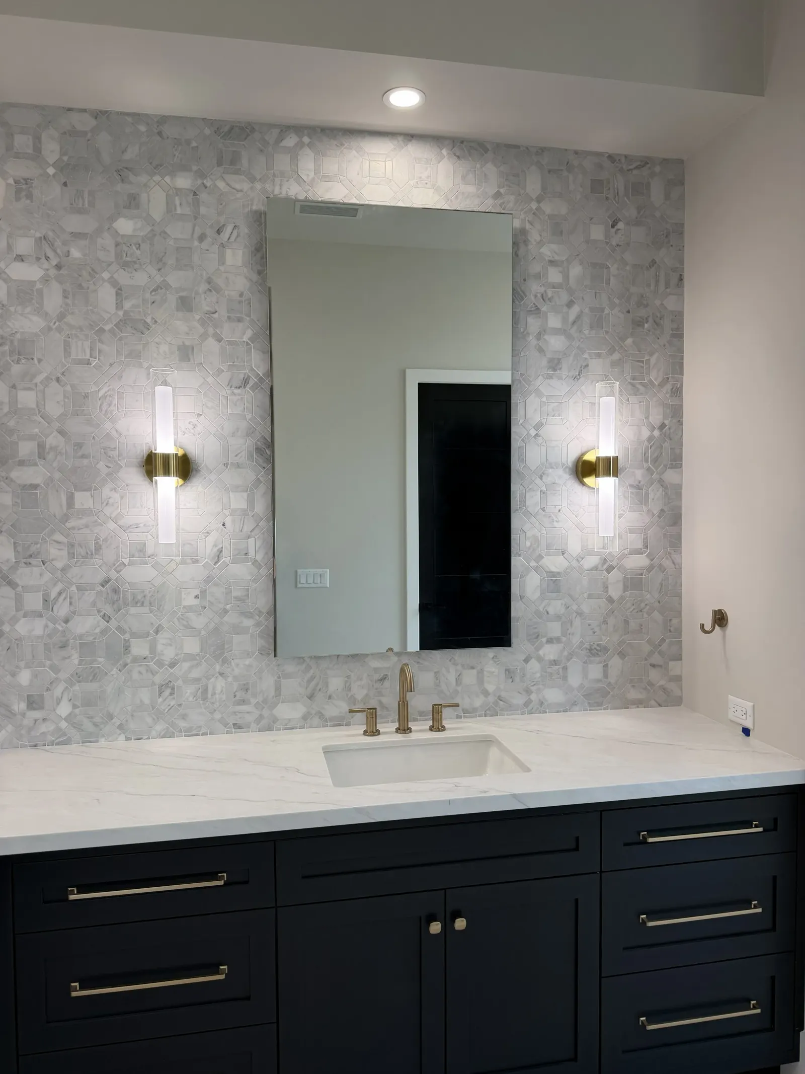 Bathroom vanity with marble mosaic wall and brass sconces